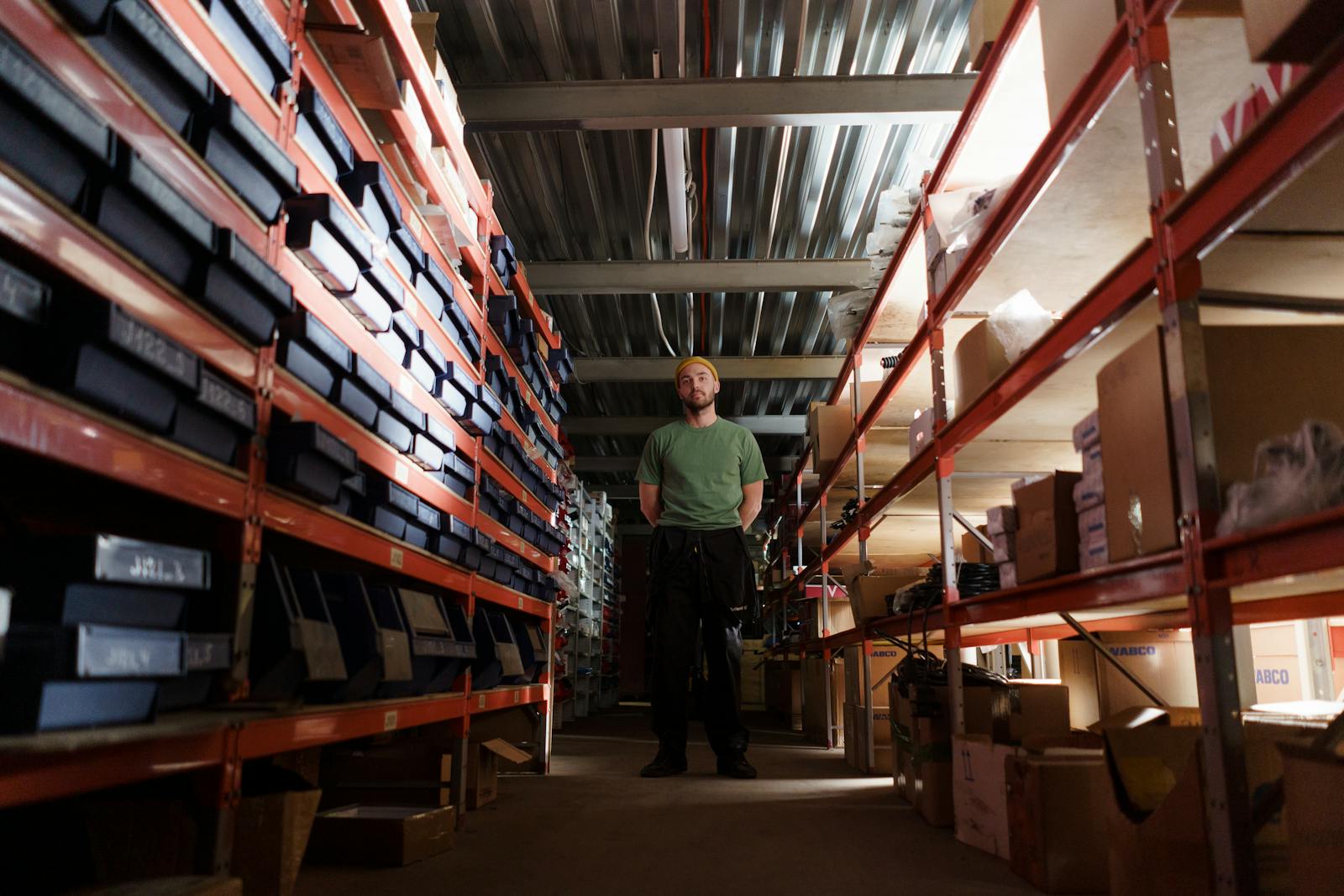 A man standing in a warehouse aisle surrounded by shelves filled with boxes and inventory.