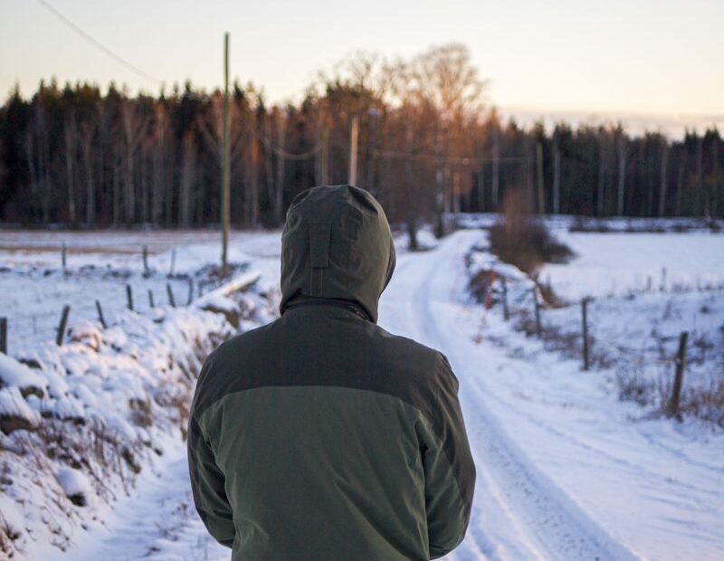 A person in a green hoodie walks on a snowy path through a serene winter landscape.